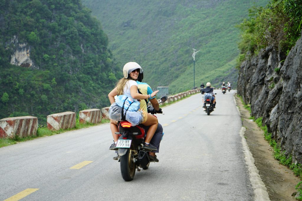 Two riders travel down a mountainous road on motorcycles, enjoying the breathtaking views of the Ha Giang loop.
